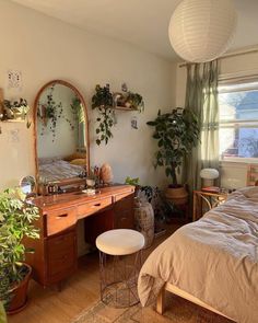 a bedroom with a bed, desk and mirror in it's corner next to potted plants