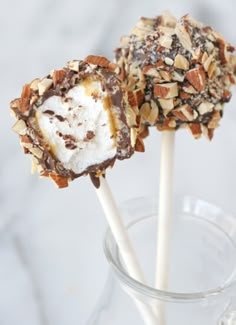 two chocolate covered marshmallows are on a stick in a clear glass cup