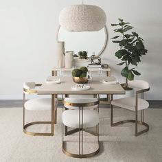 a dining table with white chairs and a round mirror above it on the wall next to a potted plant