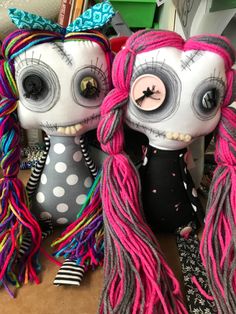 two stuffed animals with long hair and big eyes sitting next to each other on a table