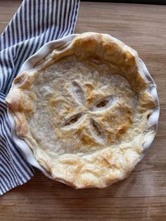 a pie sitting on top of a wooden table next to a blue and white napkin