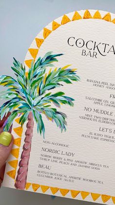 a person holding up a cocktail bar menu with a palm tree painted on it's front