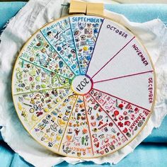 a cross stitch wheel with the names of different countries and colors on it, sitting on a piece of white fabric