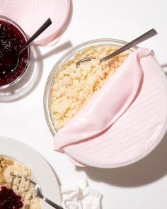 two bowls filled with food on top of a white table next to plates and spoons