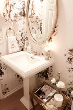 a white sink sitting under a mirror next to a table with a candle on it