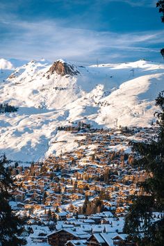 a snow covered mountain with houses in the foreground and trees on the other side