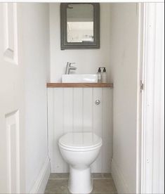 a white toilet sitting under a bathroom mirror next to a wooden shelf with a sink