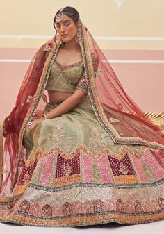 Introducing the Mehendi Green Silk Bridal Lehenga, a masterpiece of elegance and tradition. This stunning bridal lehenga features intricate zardozi embroidery with silken threads, dabka, cutdana, and sequins underlayed with multi colored velvet appliques. The green raw silk blouse perfectly complements the lehenga, while the double dupatta in matching green and contrasting crimson adds a touch of opulence. Make your wedding day truly unforgettable with this exquisite bridal wedding dress. Compos Semi-stitched Anarkali Lehenga With Meenakari, Festive Pista Green Lehenga With Cutdana, Eid Pista Green Choli With Cutdana, Eid Choli In Pista Green With Resham Embroidery, Pista Green Lehenga With Cutdana For Eid, Festive Kundan Lehenga, Raw Silk Meenakari Sharara For Reception, Pista Green Kundan Sets With Traditional Drape, Pista Green Lehenga With Zari Work For Transitional Season