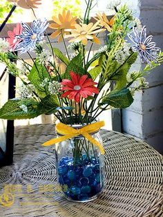 a vase filled with water and flowers on top of a wicker table next to a window