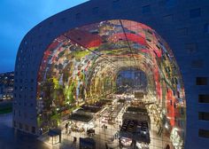 an artisticly designed building with many lights on it's sides and people walking in the street below