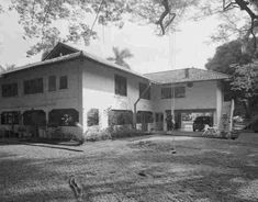 an old photo of a large house in the middle of some trees and grass with people standing outside