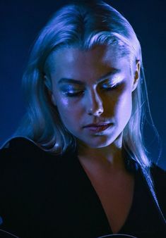 a woman with blonde hair and blue eyes playing an acoustic guitar in the dark at night