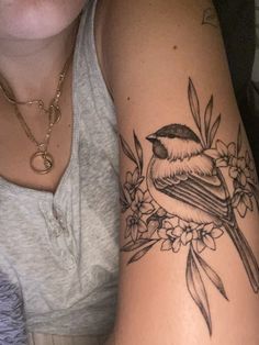 a woman's arm with a bird and flowers tattoo on the left side of her arm