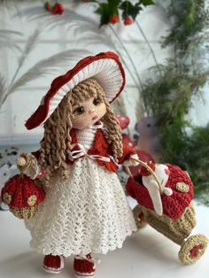 a crocheted doll with a red wagon and white dress holding a teddy bear