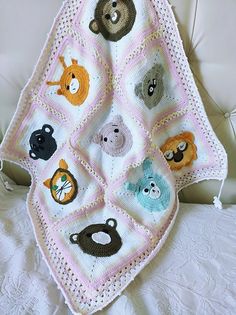 a crocheted blanket with animals on it sitting on a white chair next to a pillow