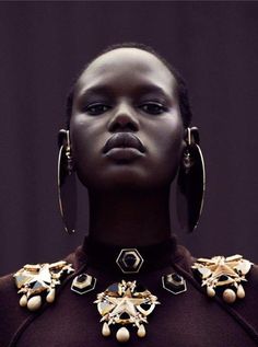 an african woman wearing large gold hoop earrings and black dress with pearls on her neck