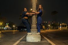 two people standing next to each other near a street light pole at night with palm trees in the background