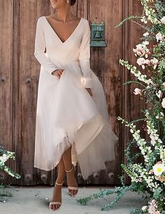 a woman standing in front of a wooden door wearing a white dress with long sleeves