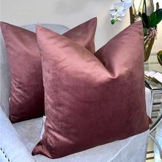 two velvet pillows sitting on top of a chair next to a vase filled with flowers