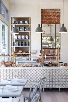 the interior of a bakery with white tables and chairs, brick walls, and open shelving