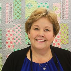 a woman standing in front of a quilt with flowers on the wall behind her smiling