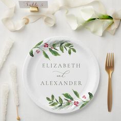 a white plate with greenery on it next to gold utensils and napkins