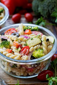 two bowls filled with pasta salad on top of a cutting board next to tomatoes and broccoli