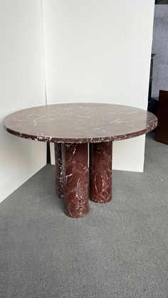 a round marble table sitting in front of a white wall with two red pillars on it