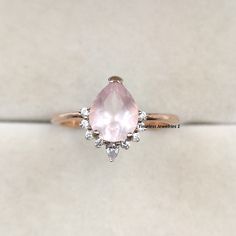 an engagement ring with a pink stone surrounded by white diamonds on a plain surface,