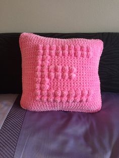 a pink crocheted pillow sitting on top of a bed