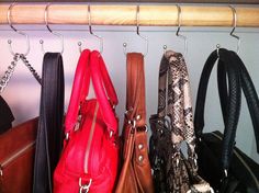 several purses are hanging on a rack in the closet, with one being held by a metal hook