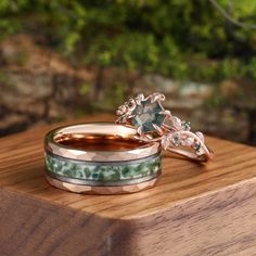 two wedding rings sitting on top of a wooden table next to another ring with green and white stones