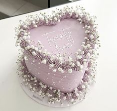 a heart shaped cake with white flowers on the top and purple frosting in the middle