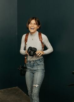 a woman holding a camera and smiling while standing in front of a wall with green walls