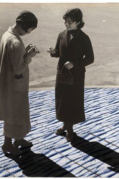 two women standing next to each other on top of a tarp covered roof looking at something in their hands