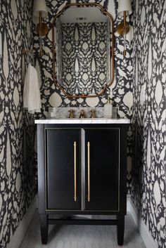 a bathroom with black and white wallpaper, gold accents and a mirror above the sink