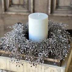 a white candle sitting on top of an old book next to a wreath with dried flowers