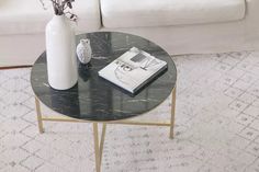 a table with a book and vase on it in front of a white couch next to a coffee table