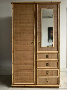 an antique bamboo armoire with drawers and mirror on the front, against a white wall