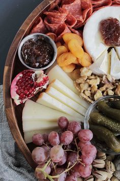 a wooden platter filled with cheese, crackers, grapes, nuts and fruit