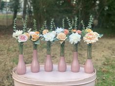 six pink vases with flowers in them sitting on a white table outside by some trees