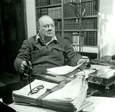 an old man sitting at a desk with lots of books and papers in front of him