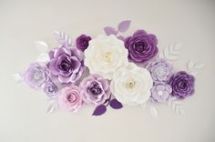 purple and white paper flowers are arranged on the side of a wall in an arrangement