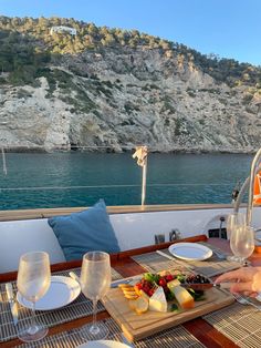 a woman sitting at a table on top of a boat with food and wine in front of her