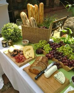 an assortment of cheeses, bread and grapes on a table with other food items