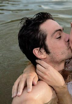 a man and woman are in the water kissing each other while they both have their heads close to one another