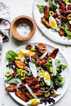 two plates filled with salad on top of a white table next to a wooden bowl