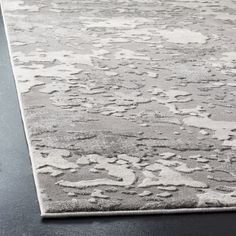 an area rug with white and gray designs on the ground, in front of a black table