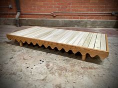 a wooden bench sitting on top of a cement floor next to a red brick wall