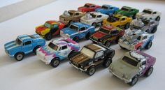 many toy cars are lined up on a white table top, with one car painted in different colors